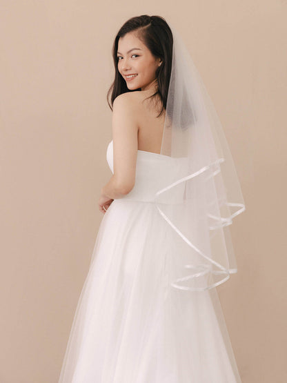 Woman wearing a white wedding dress with a veil against a beige background