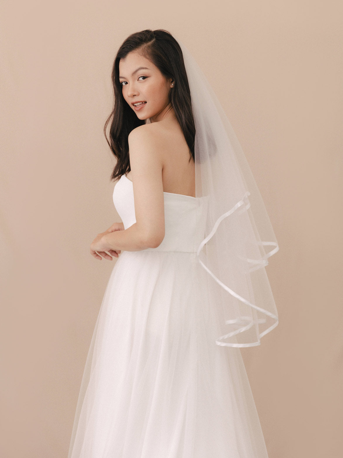 Woman wearing a white wedding dress with a veil against a beige background