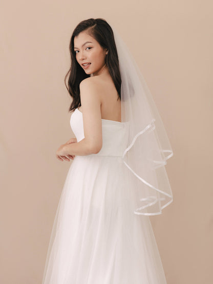 Woman wearing a white wedding dress with a veil against a beige background