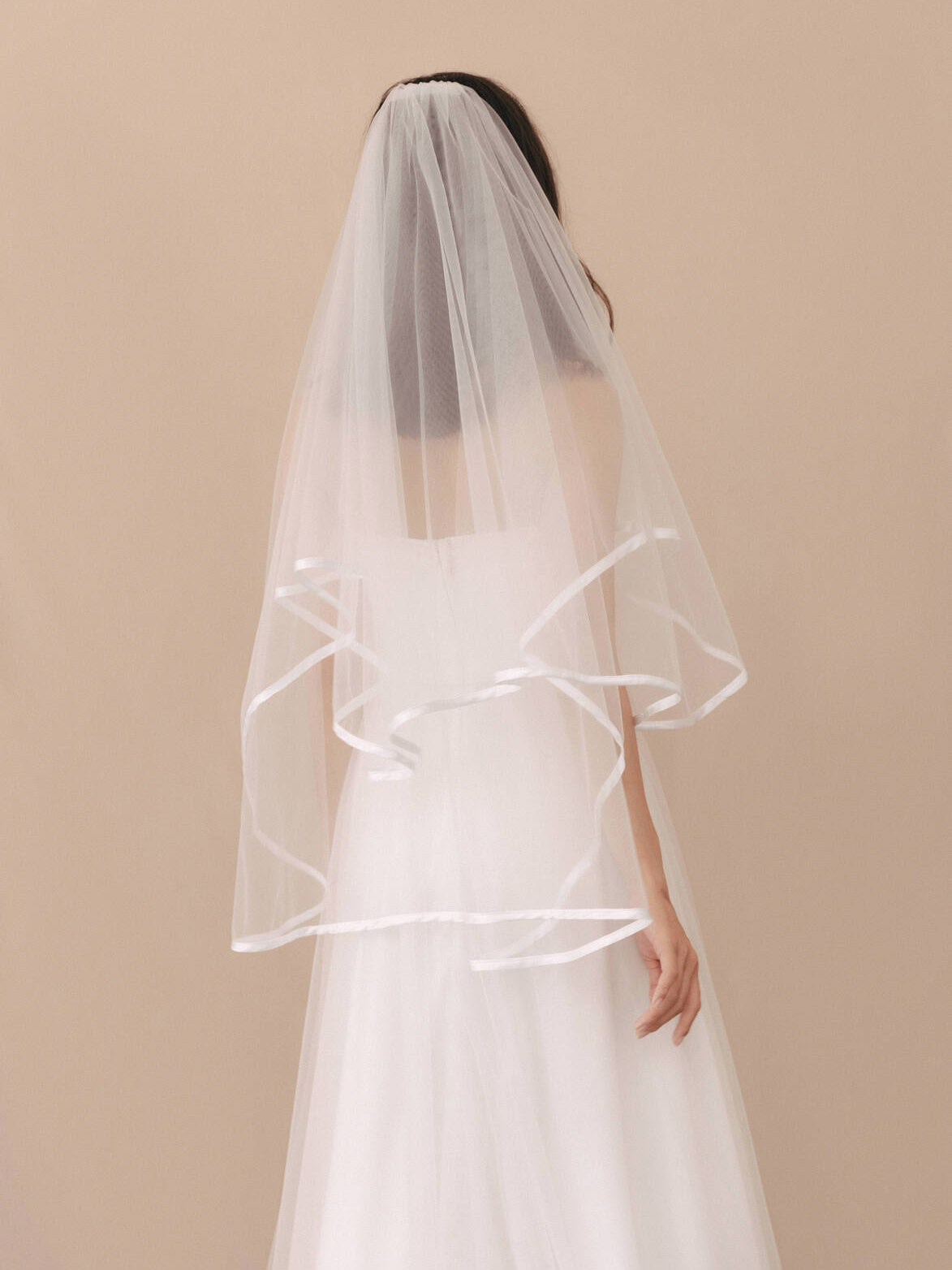 White wedding dress with a long veil on a beige background