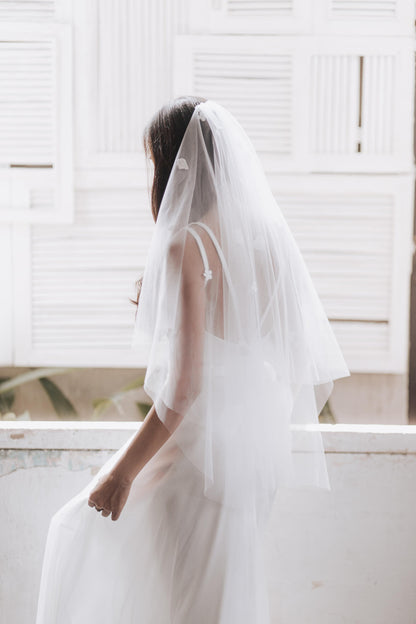 Person wearing a white wedding dress with a veil in a bright room.