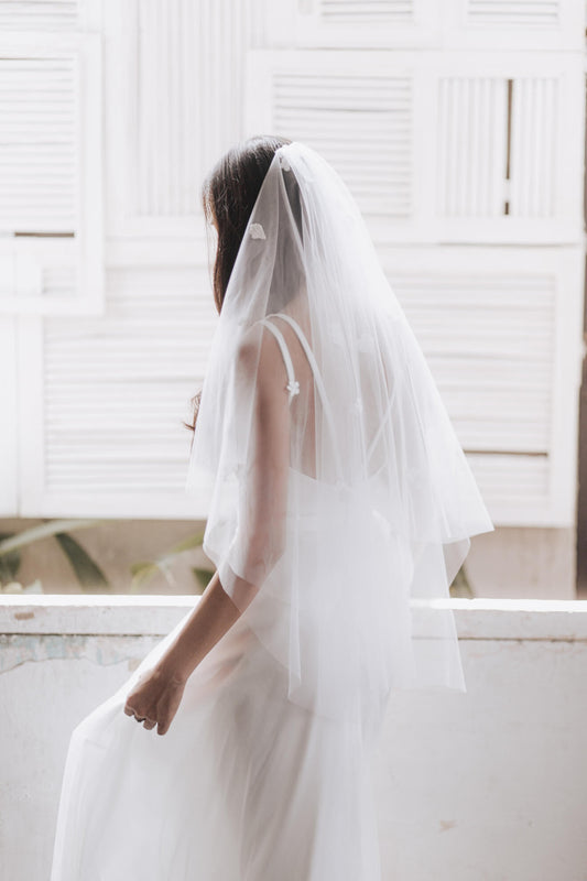 Person wearing a white wedding dress with a veil in a bright room.