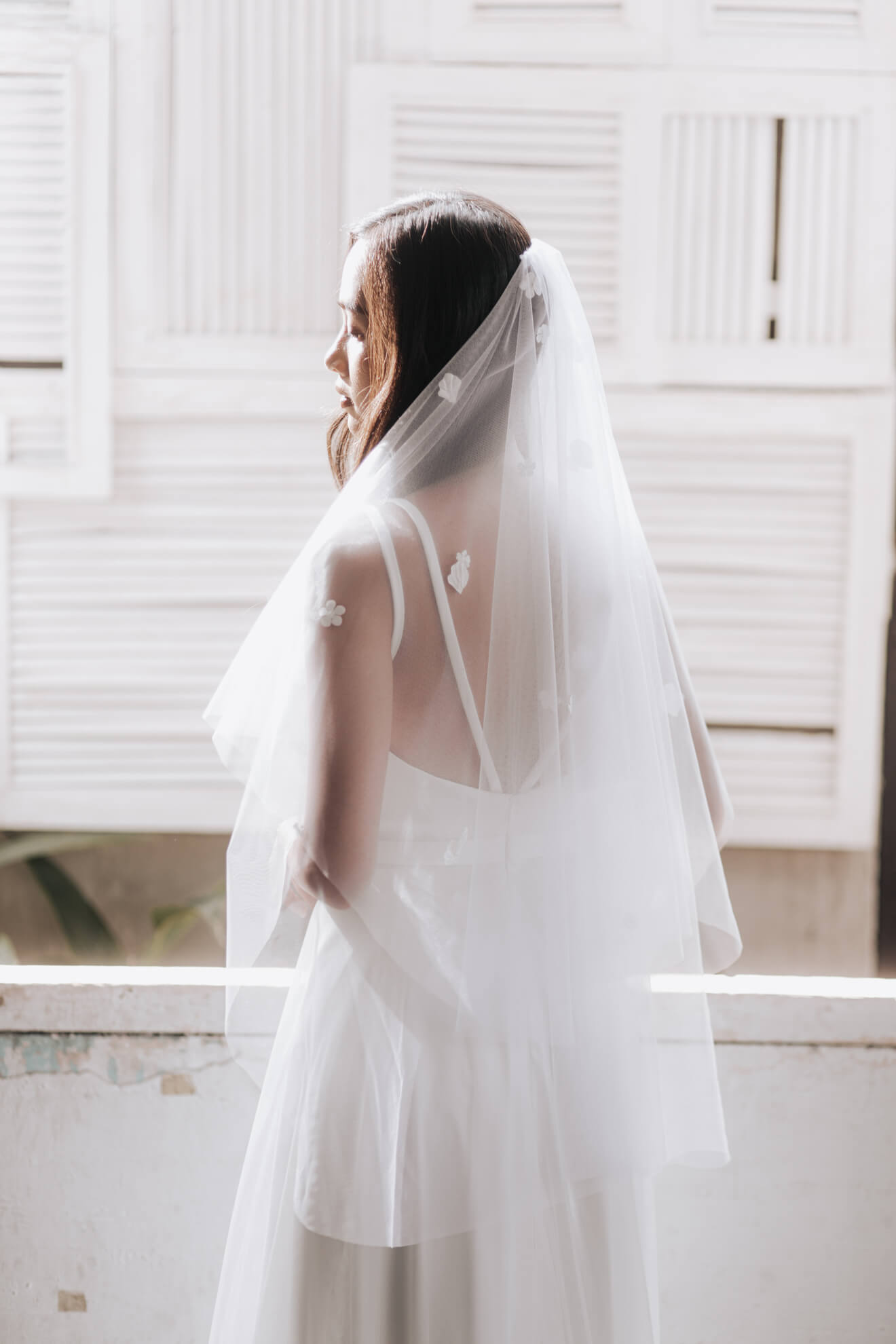 Bride wearing a white wedding dress with a veil in a bright room.
