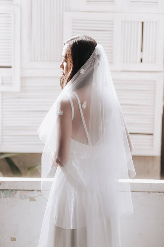 Bride wearing a white wedding dress with a veil in a bright room.