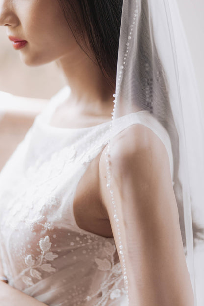Close-up of a person wearing a white lace wedding dress with a veil.