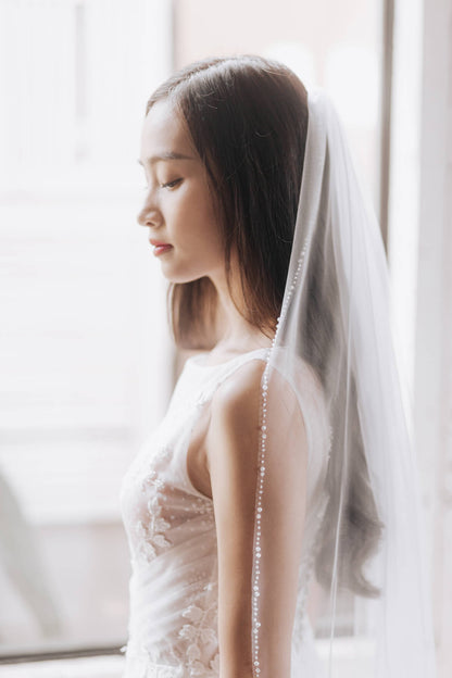 Woman wearing a white wedding dress with a veil in a softly lit room.