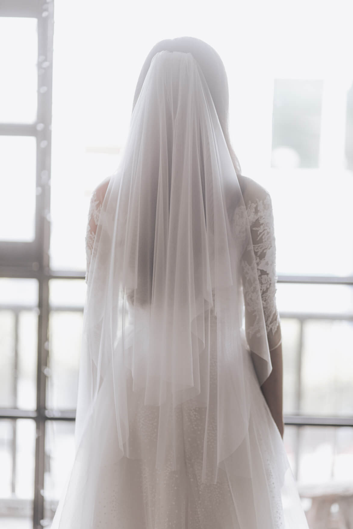 Person wearing a long, light-colored veil in front of a window.