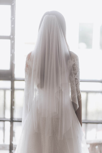 Person wearing a long, light-colored veil in front of a window.
