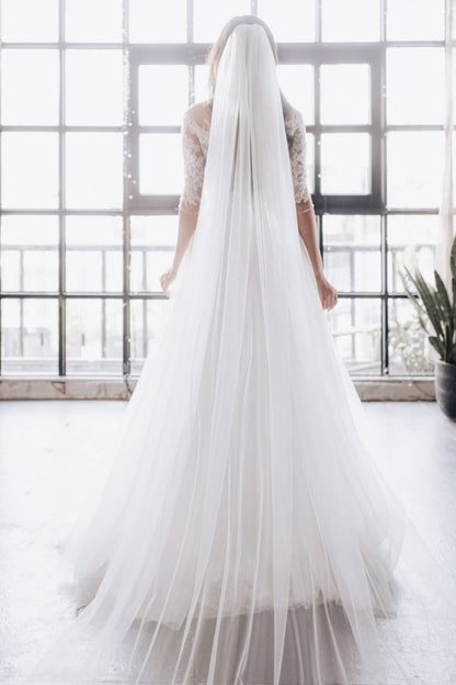 Person wearing a long white wedding dress with a flowing train indoors.