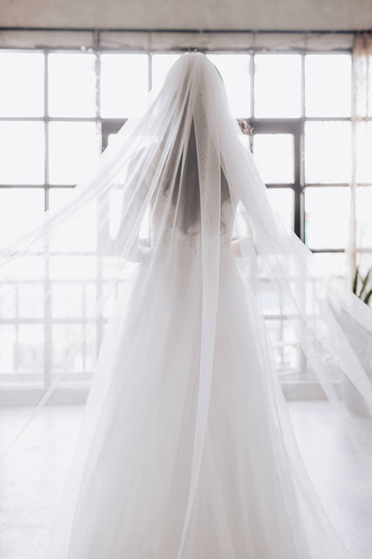 White wedding dress with a long train in front of a window