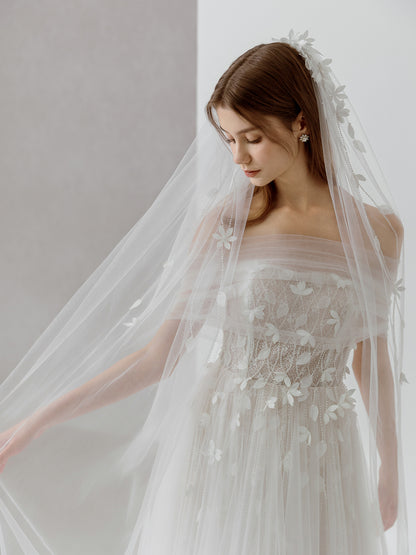 Woman wearing a lace wedding dress with a long veil against a plain background