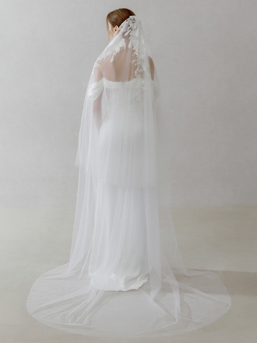 Woman wearing a white wedding dress with a long veil against a plain background