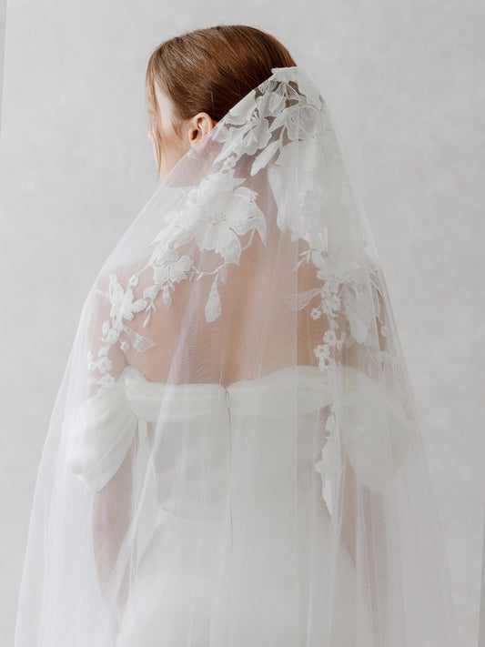 Woman wearing a white lace veil against a plain background