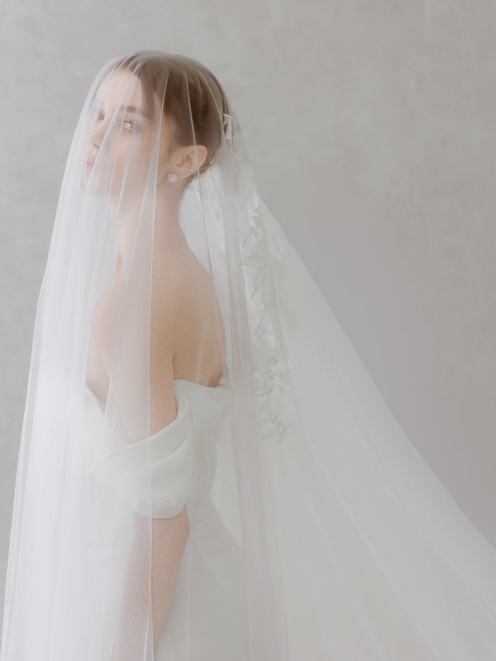 Woman wearing a white wedding dress with a long veil against a plain background