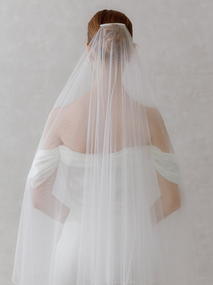 Person wearing a white wedding dress with a veil against a plain background