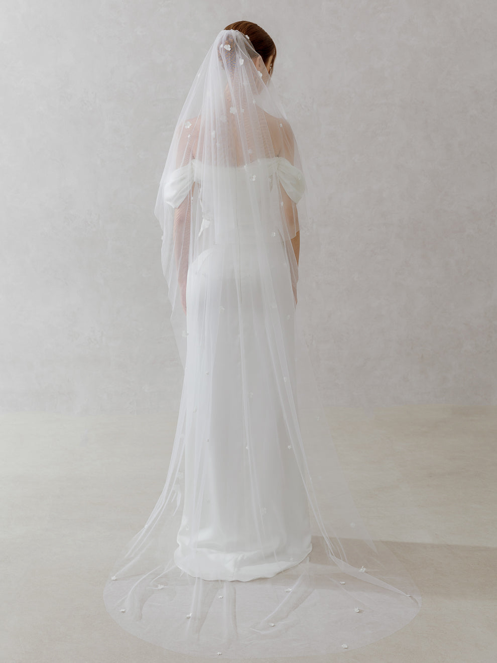 Woman wearing a white wedding dress with a long veil against a plain background