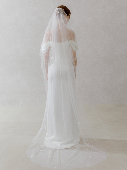 Woman wearing a white wedding dress with a long veil against a plain background