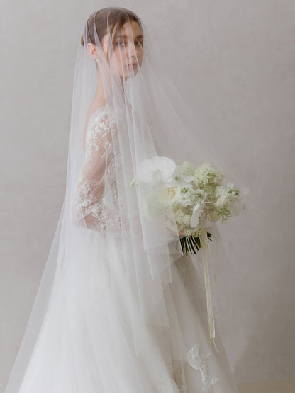 Bride in a white wedding dress with a veil and bouquet against a plain background