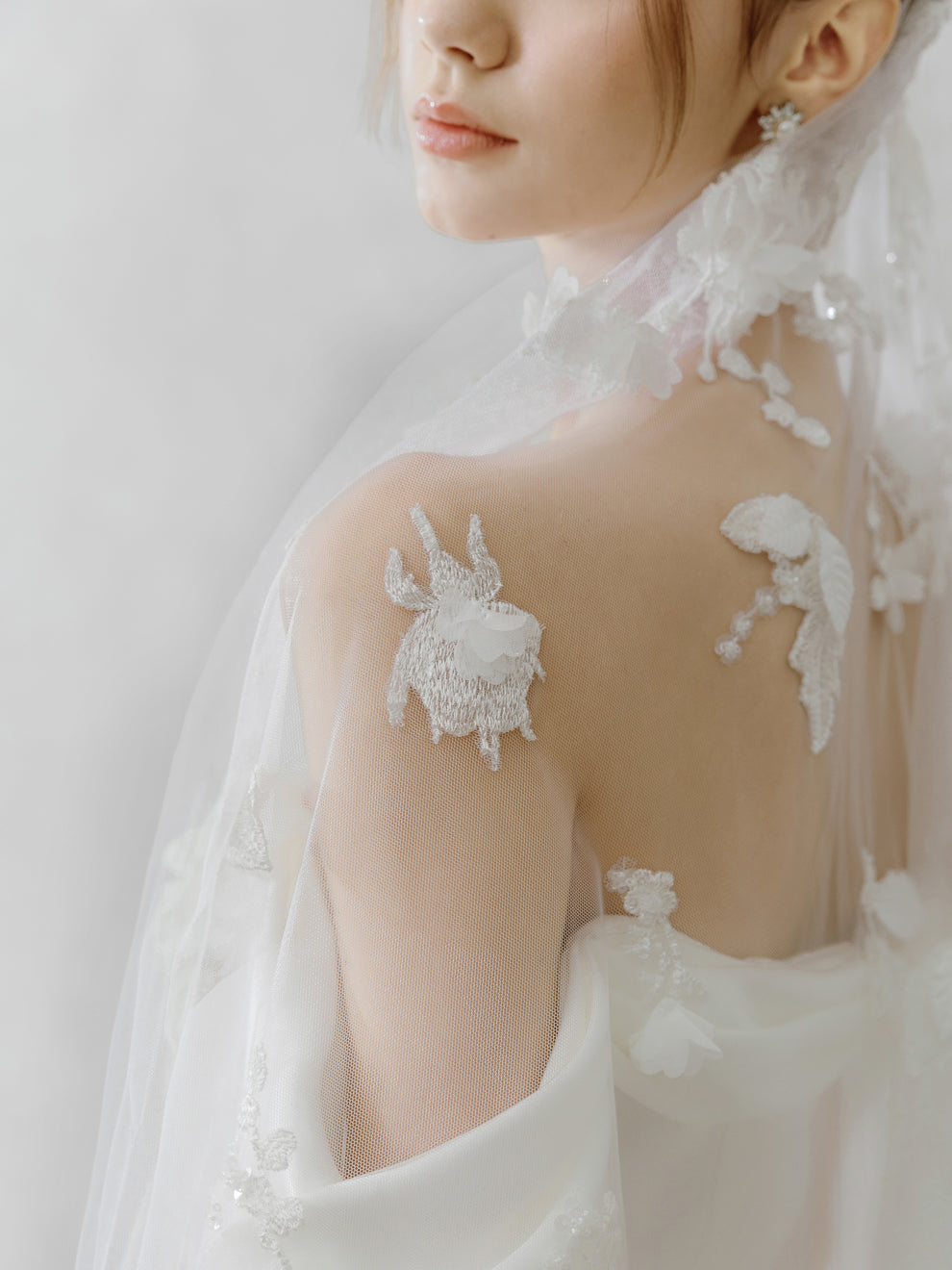 Close-up of a person wearing a white lace wedding dress with a plain background