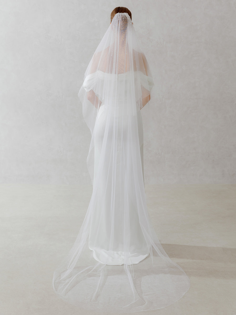 White wedding dress with a long train and veil on a plain background
