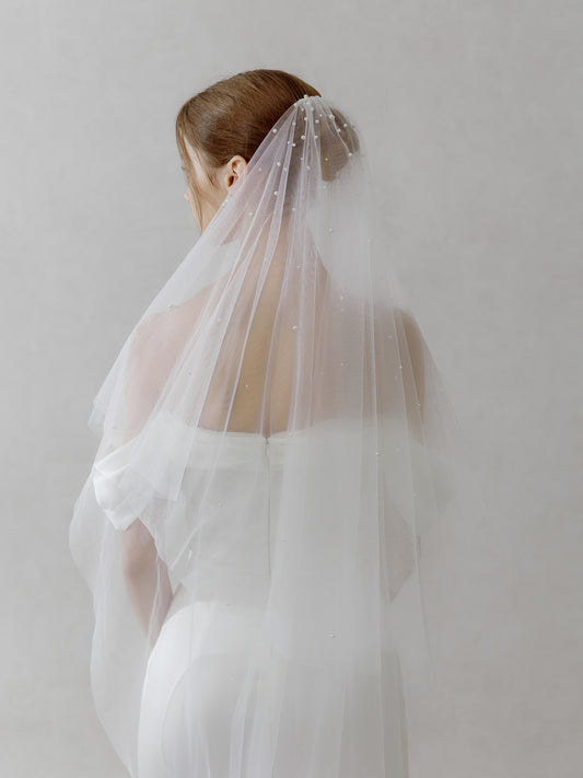 Woman wearing a white wedding dress with a veil against a plain background
