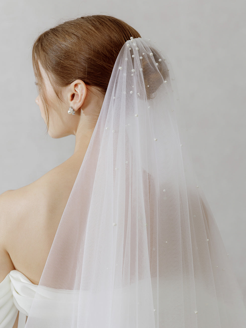 Woman wearing a light pink veil with a subtle pattern on a plain background