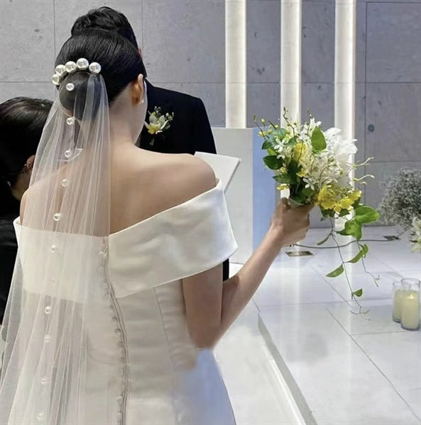 Bride wearing a 1.2m long bridal veil adorned with large pearl beads, paired with an off-the-shoulder wedding gown during a ceremony.