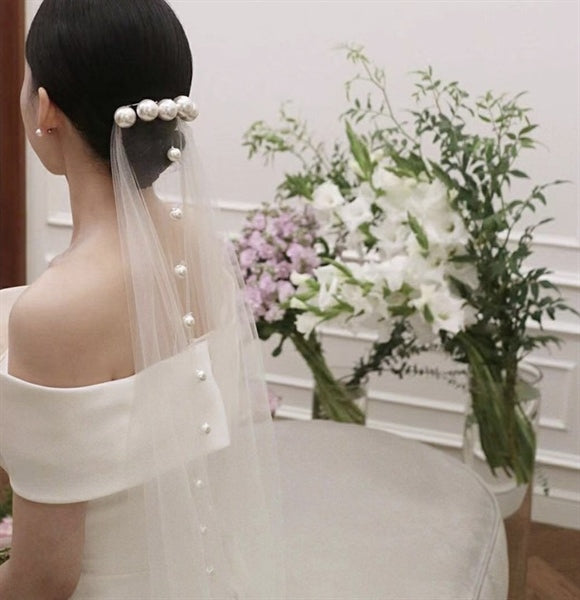 Bride wearing a 1.2m long bridal veil adorned with large pearl beads, paired with an off-the-shoulder wedding gown during a ceremony.