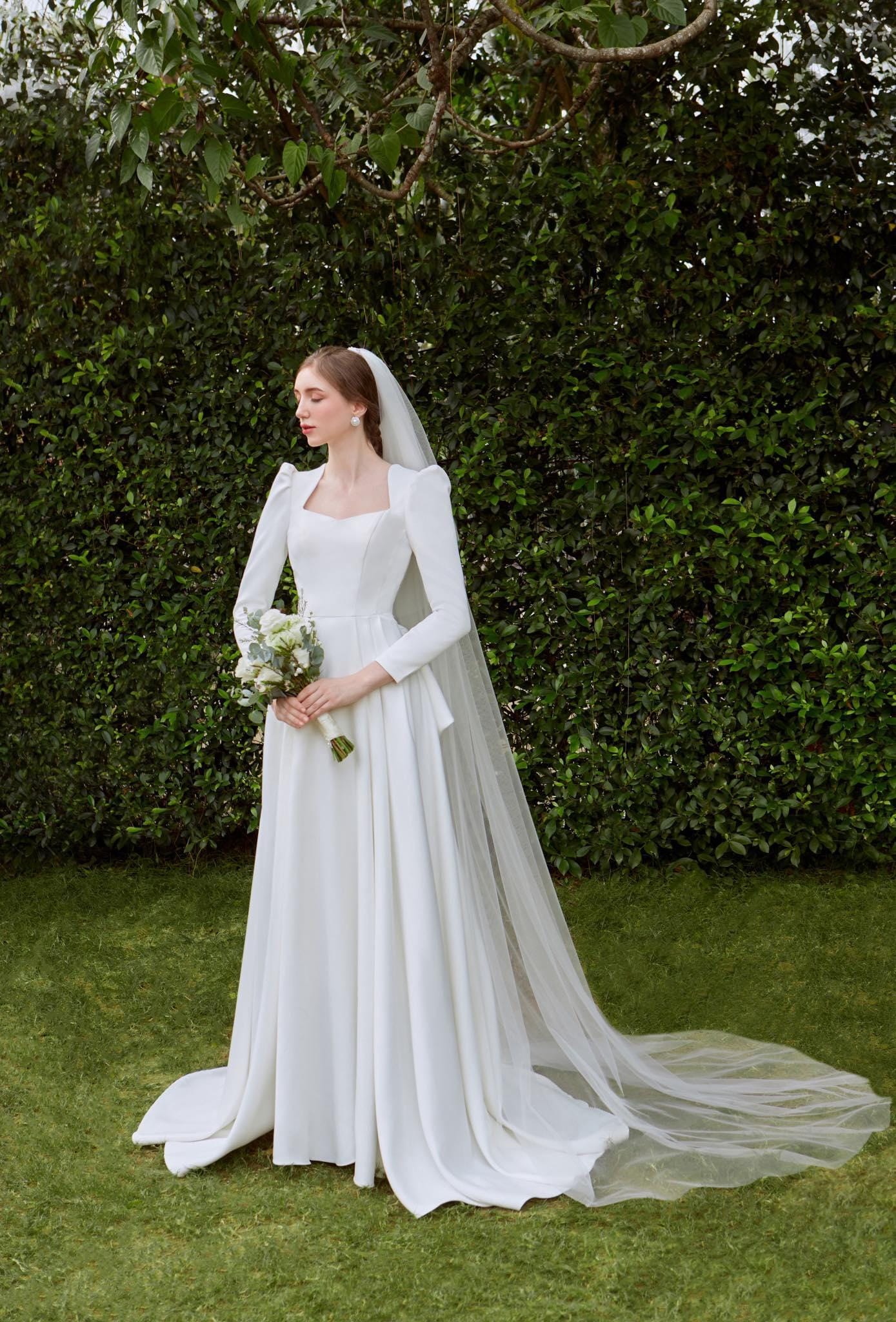 Bride wearing a Classic Cathedral-Length Veil, standing gracefully with a bouquet in a garden setting.