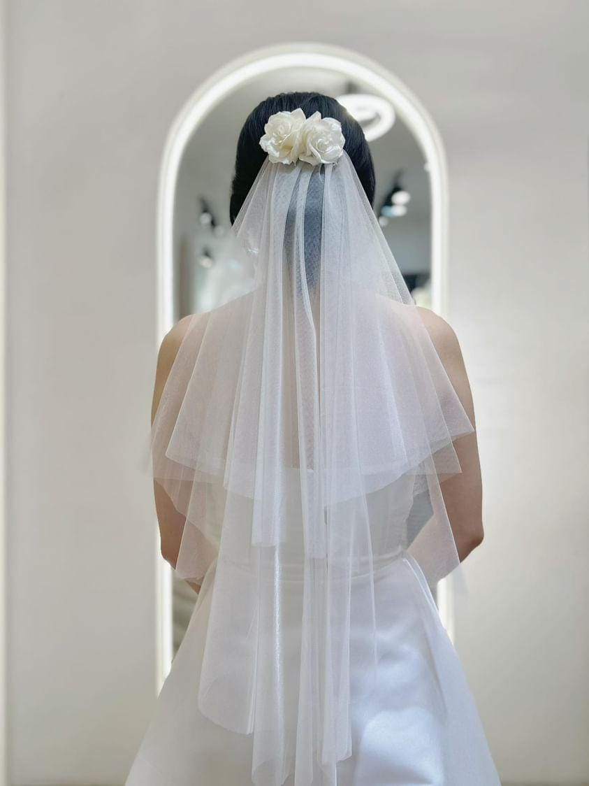 Bride wearing a Chic Tiered Veil with a floral hairpiece, showcasing layered tulle design in a bridal boutique.