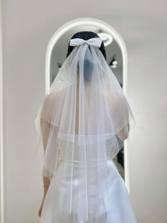 Bride wearing an Elegant Tiered Veil with a classic satin bow, showcasing layered tulle design in a bridal boutique.