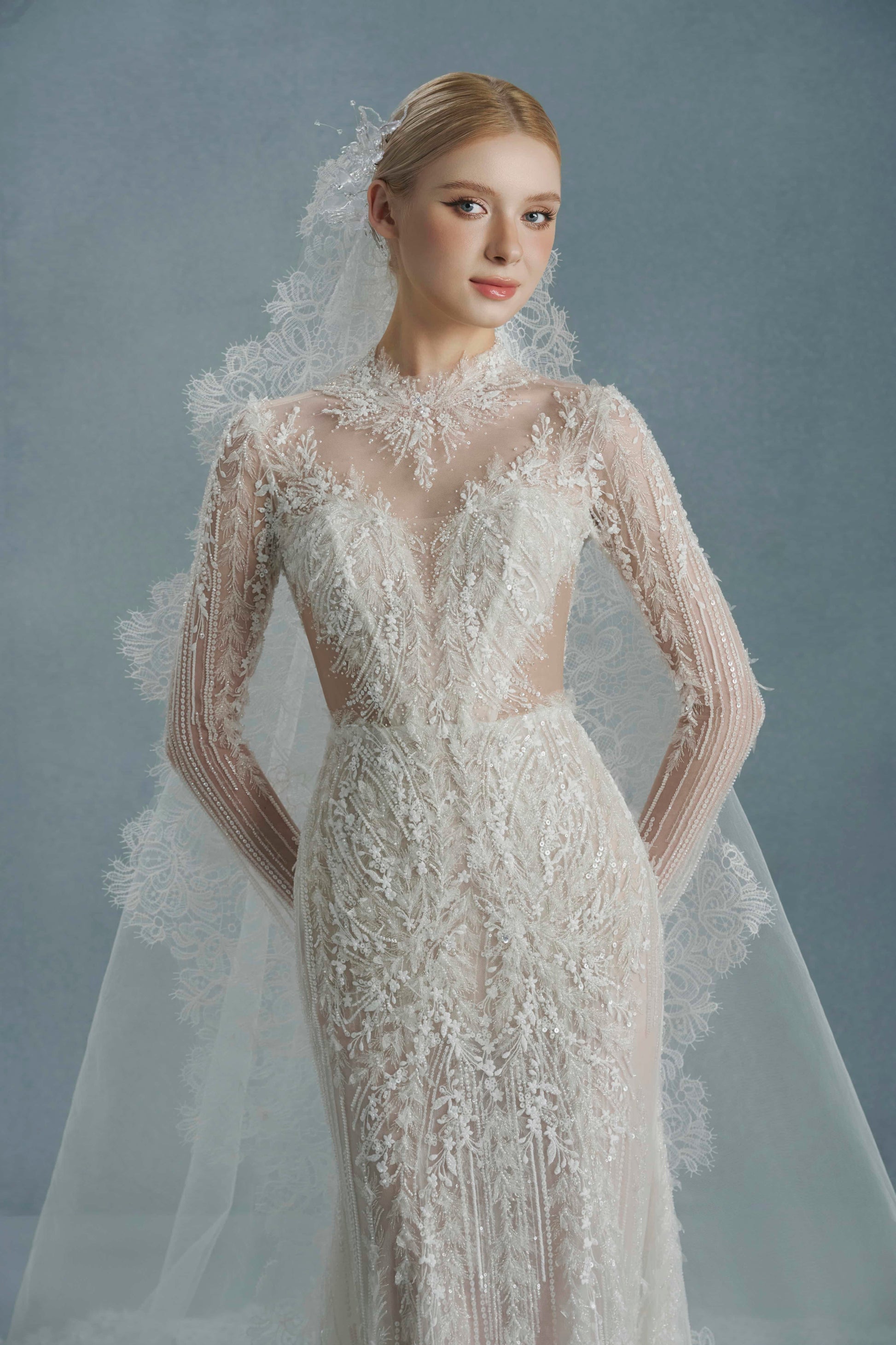Woman wearing a lace wedding dress with a long veil against a gray background