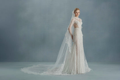 Woman wearing a white lace wedding dress with a long train against a gray background