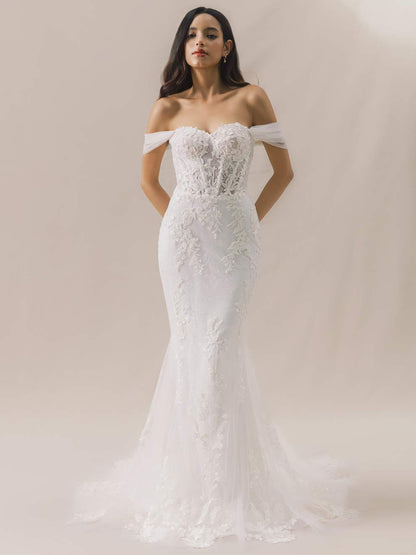 Woman wearing a white off-shoulder lace wedding dress against a plain background