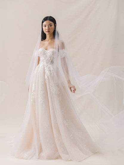Model wearing a white wedding dress with floral details against a plain background