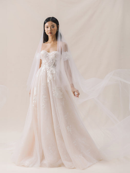Model wearing a white wedding dress with floral details against a plain background