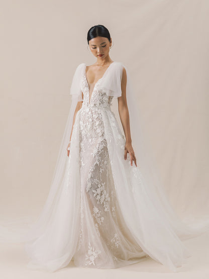 Woman wearing a white lace wedding dress against a plain background