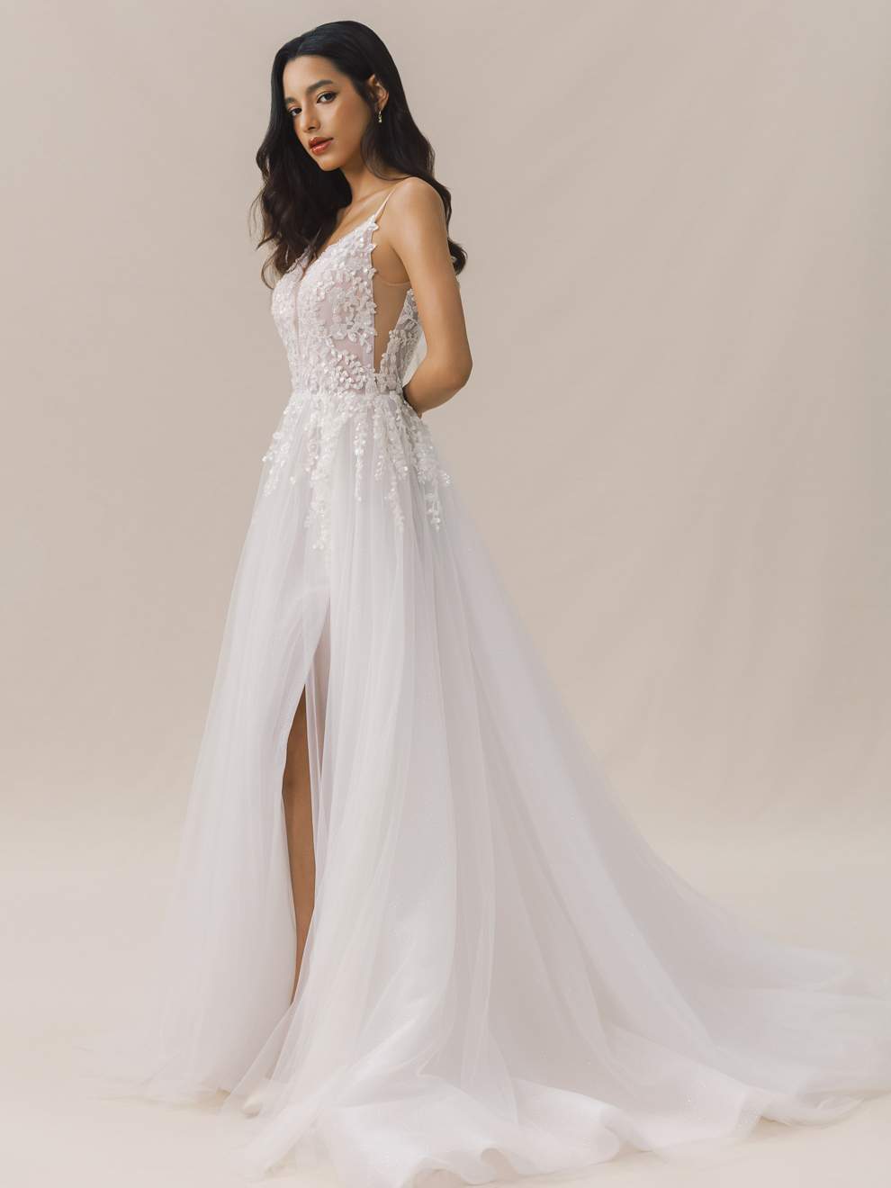 Woman wearing a white lace wedding dress with a high slit on a plain background