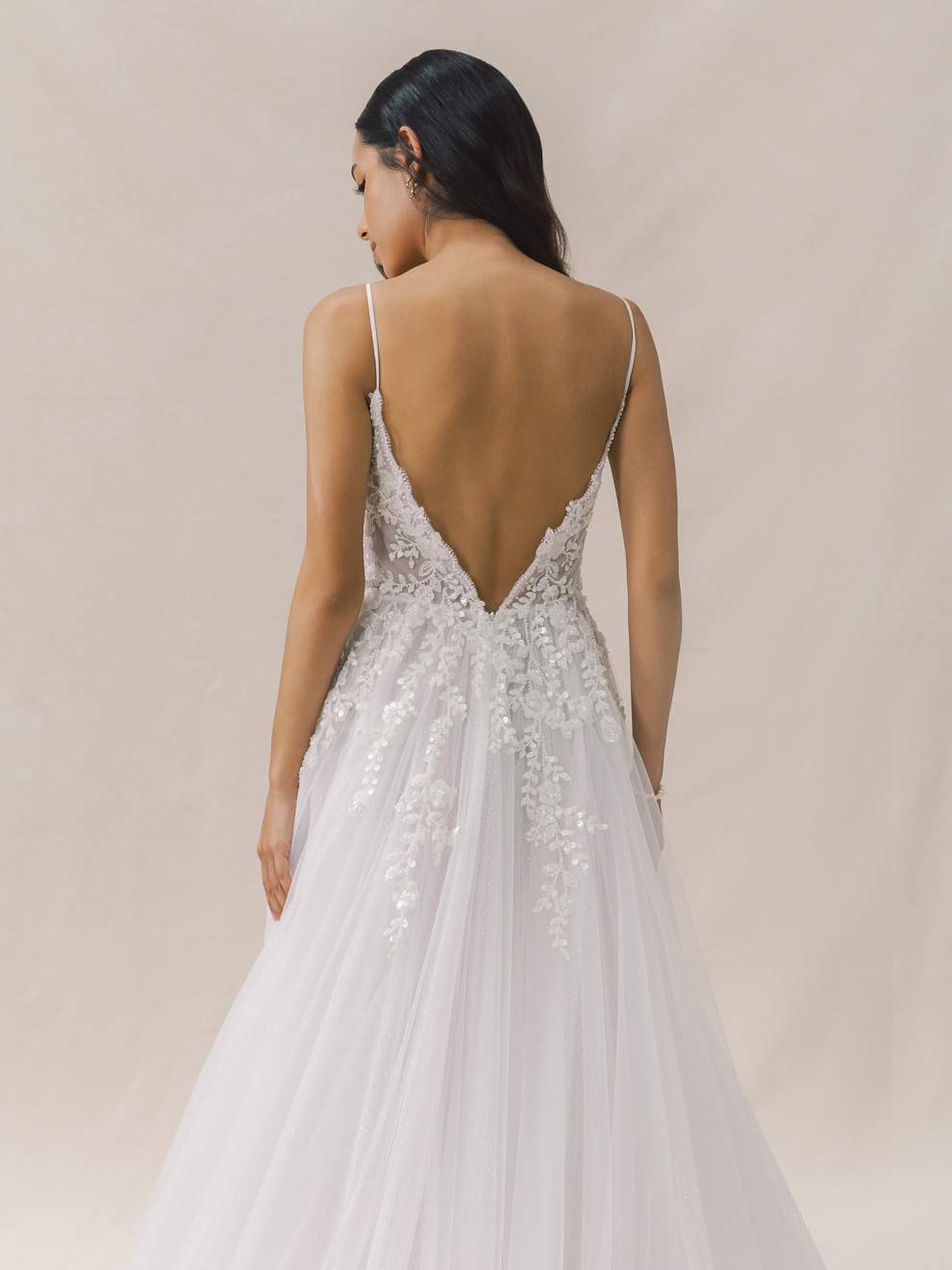 Woman wearing a white wedding dress with a low back on a beige background
