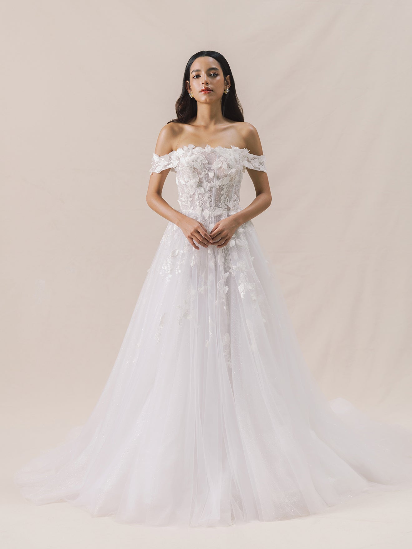 Woman wearing a white off-shoulder wedding dress with floral details on a beige background