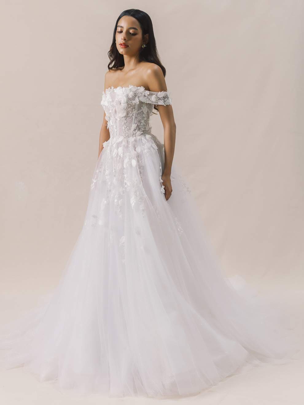Woman wearing a white floral off-shoulder wedding dress against a plain background