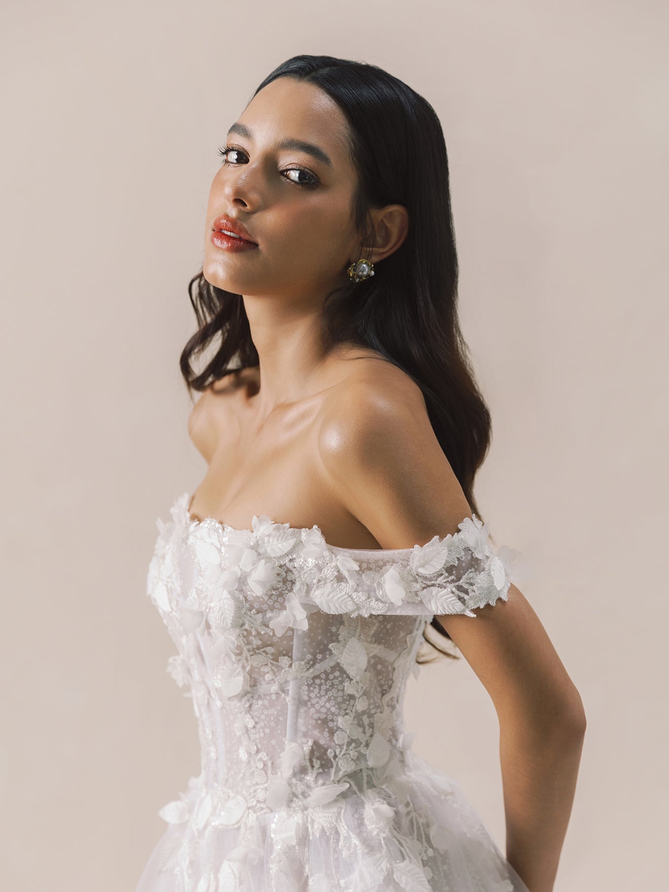 Woman wearing a white off-shoulder lace dress against a beige background