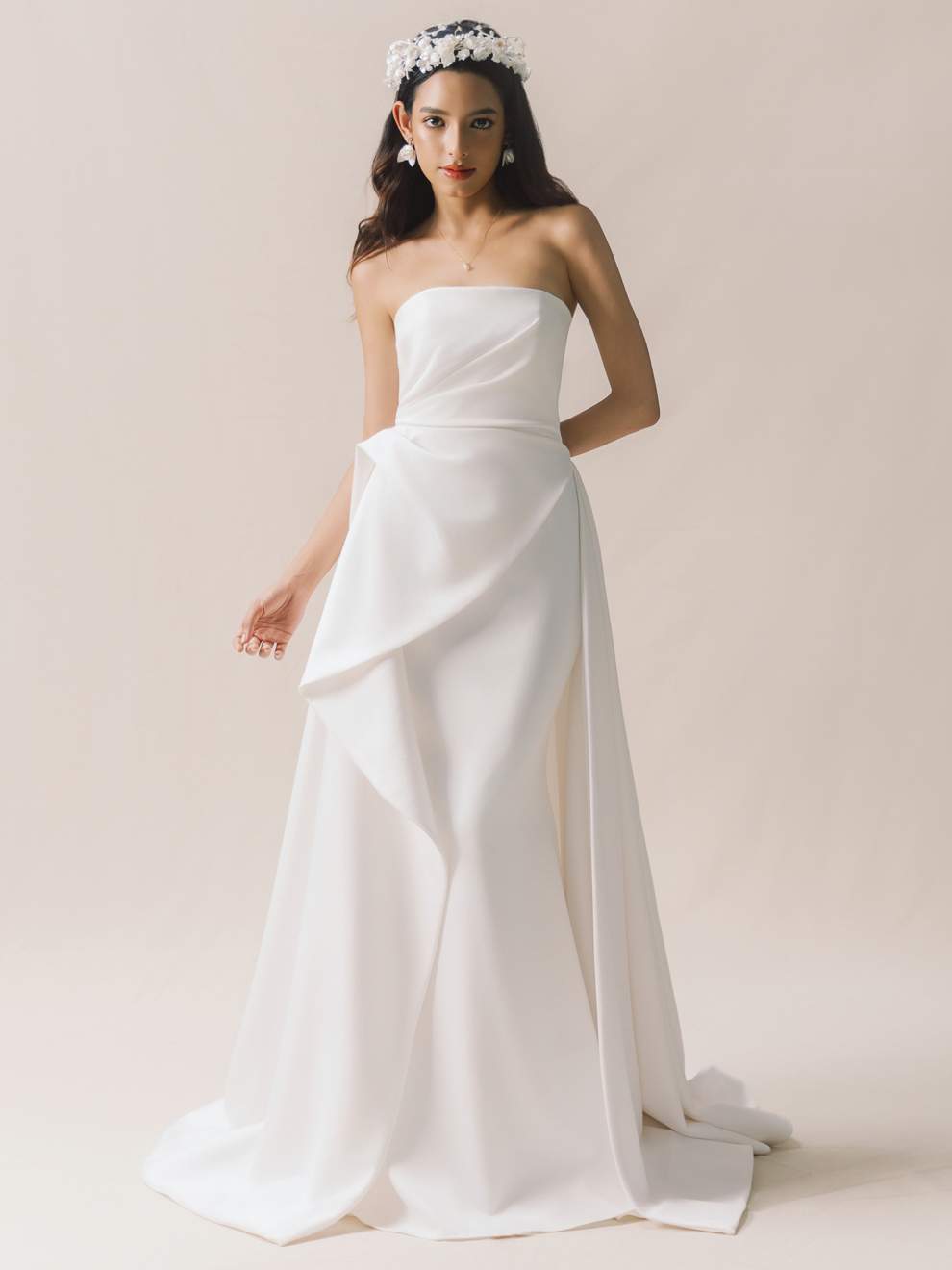 Woman wearing a strapless white wedding dress with a slit on a plain background
