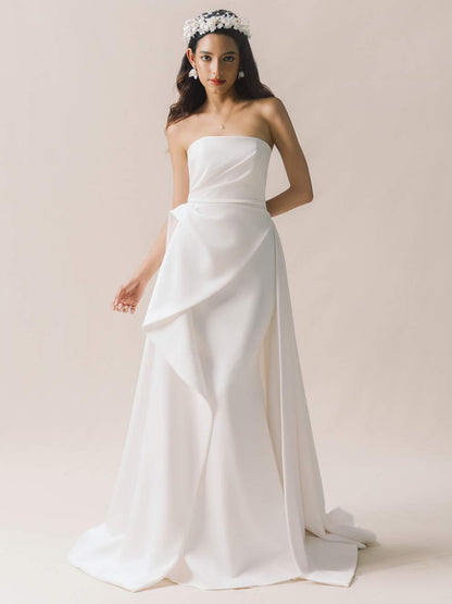 Woman wearing a strapless white wedding dress with a slit on a plain background