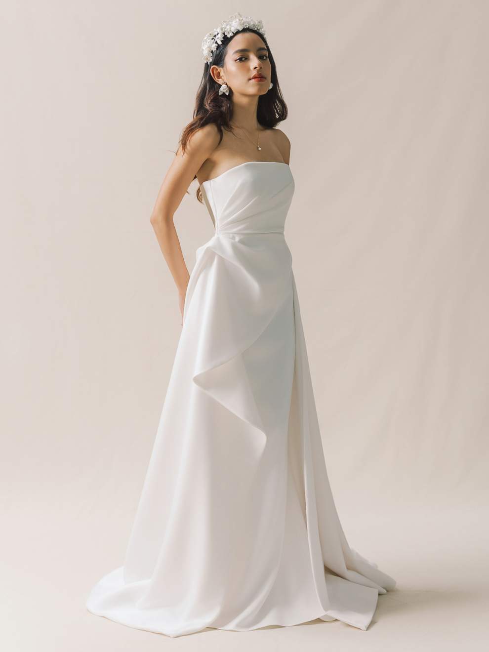 Woman wearing a strapless white wedding dress against a plain background