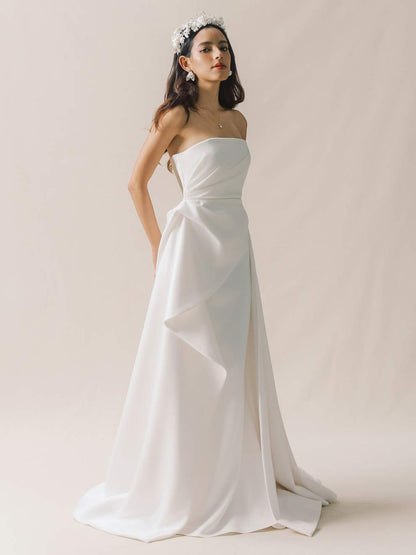Woman wearing a strapless white wedding dress against a plain background