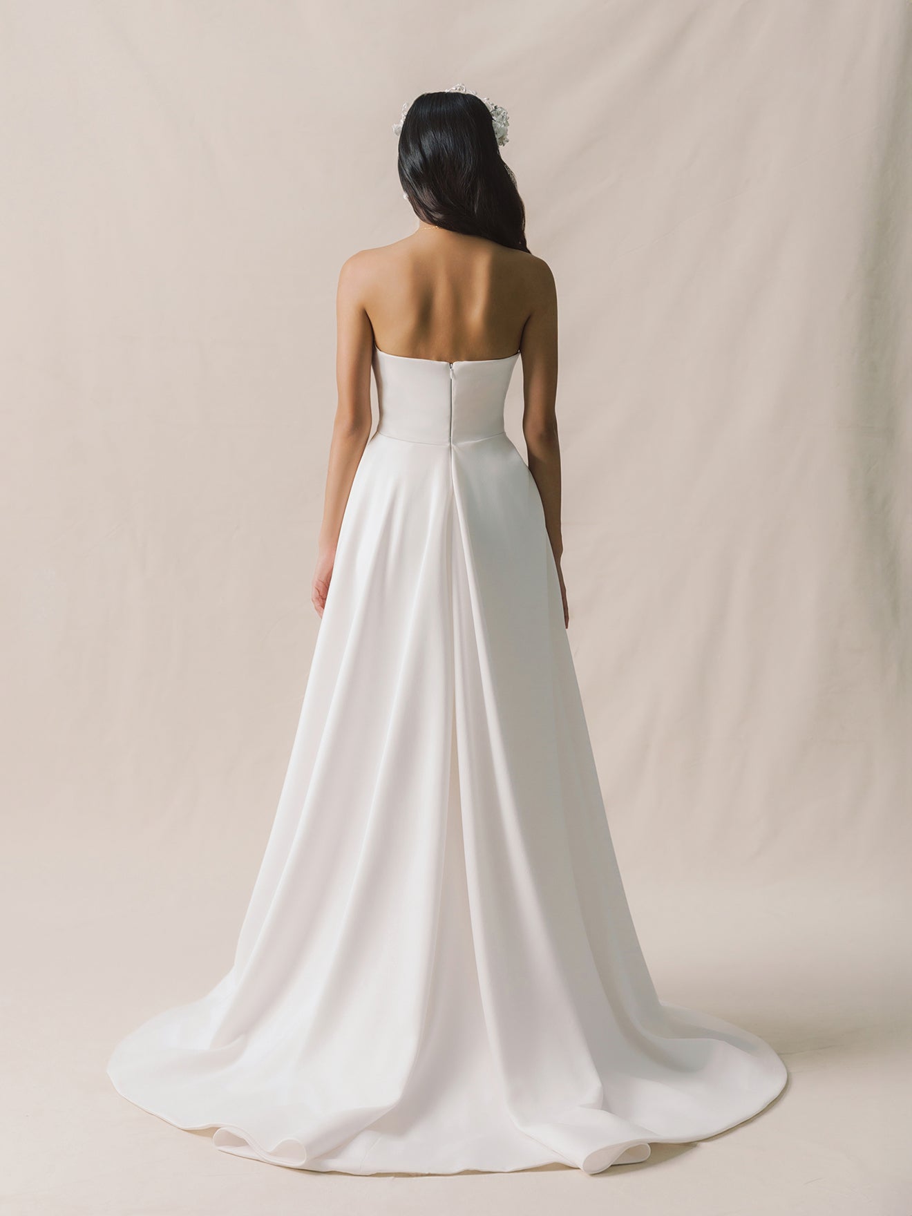 Woman wearing a strapless white wedding dress against a beige background