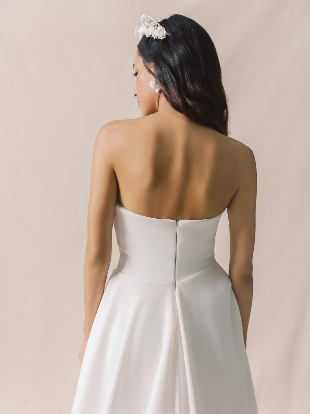 Woman wearing a strapless white wedding dress with a plain background