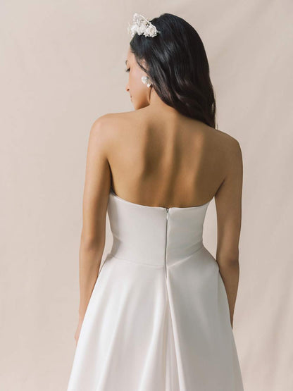 Woman wearing a strapless white wedding dress with a plain background