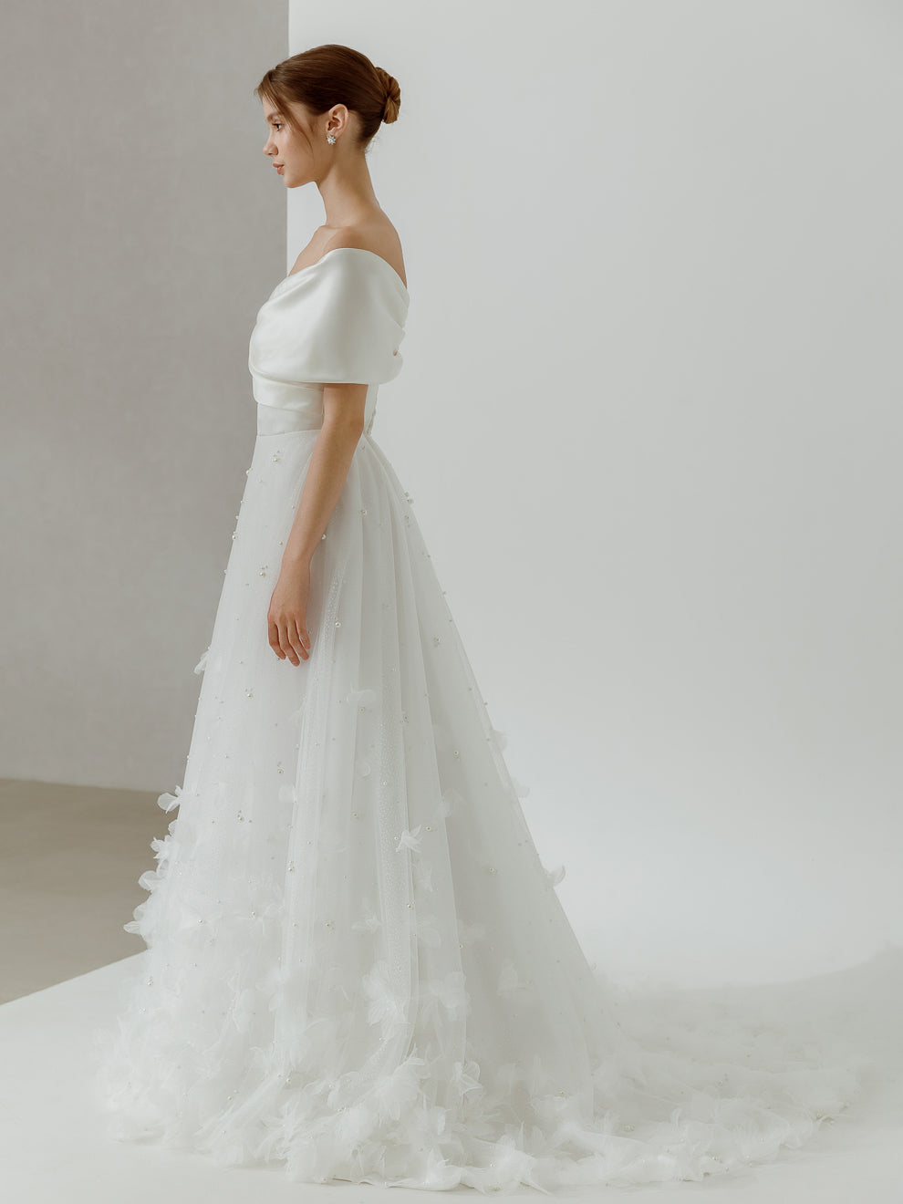 Woman wearing a white wedding dress with a soft, flowing skirt against a plain background